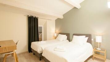 A hotel room with two beds, a wooden table, and a nightstand with a lamp.