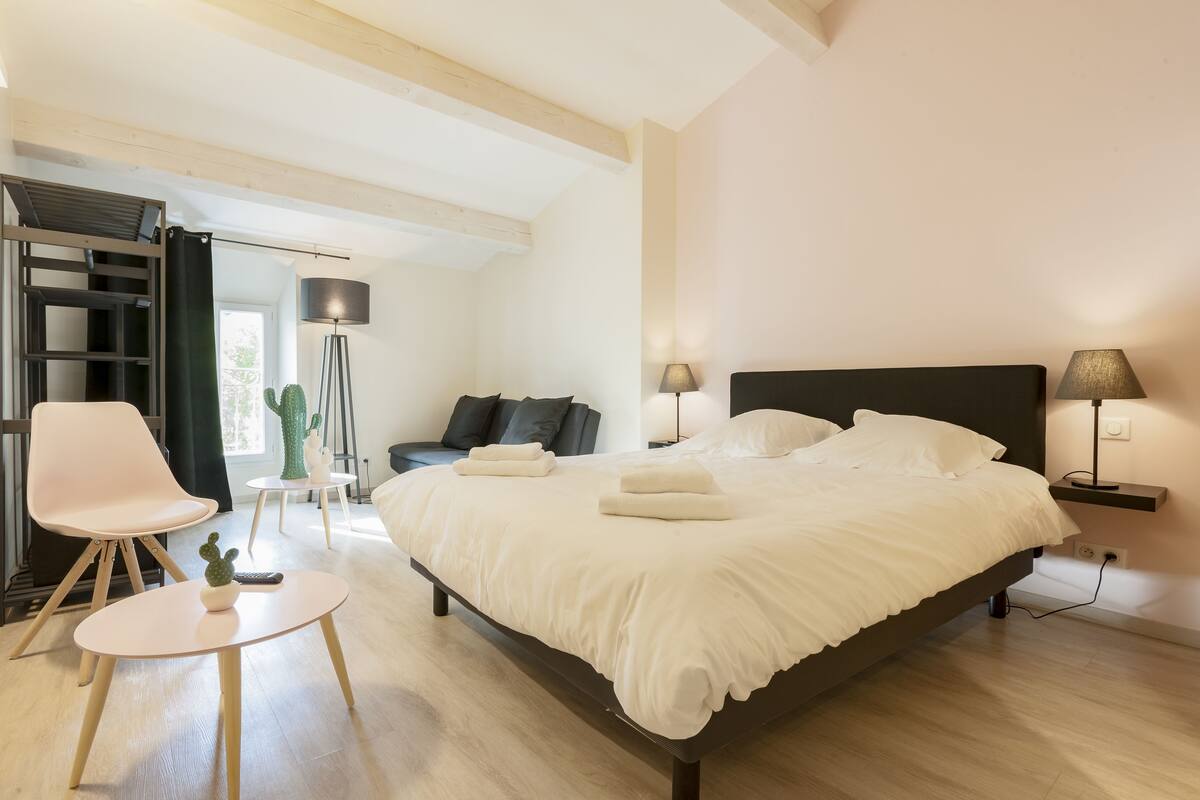 A modern bedroom with a large bed, a desk, a chair, and a lamp.