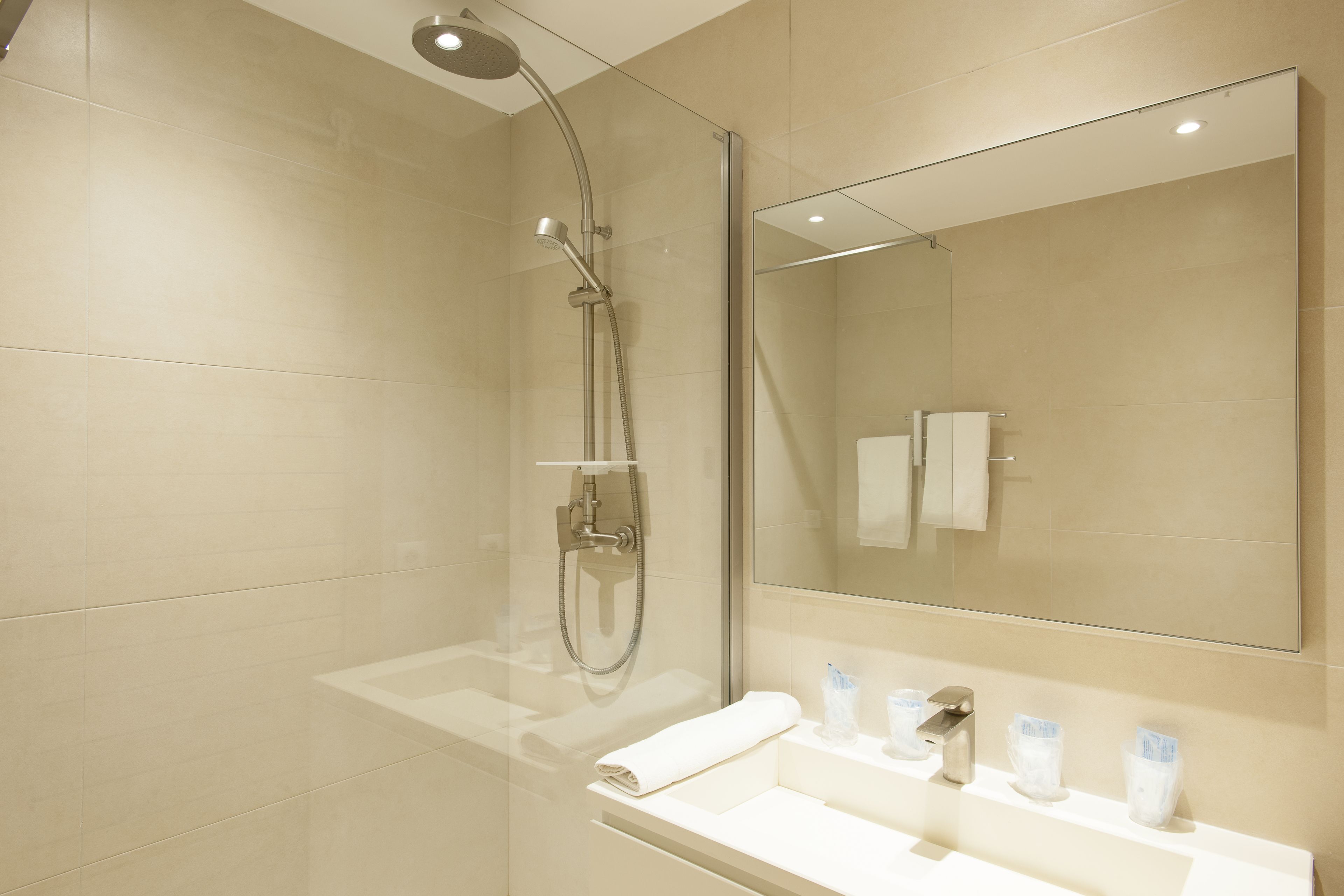 A modern bathroom with a glass-enclosed shower, a large mirror, and a white sink with toiletries.