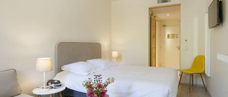 Una habitación de hotel con una cama, una mesita con lámpara, una silla y un florero con flores.