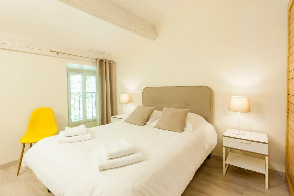 Un lit bien fait, avec du linge de lit blanc, une chaise jaune vif et deux tables de chevet avec des lampes.