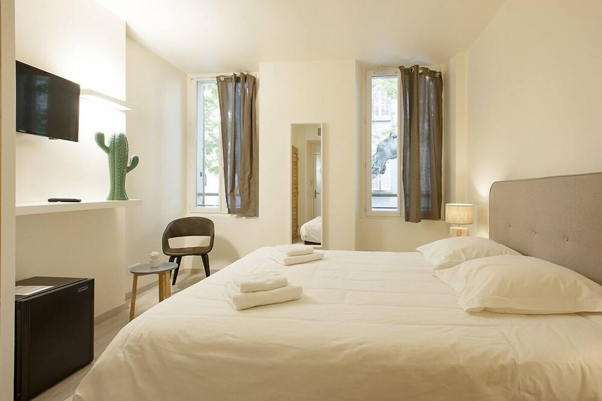 A hotel room with a bed, a desk, a chair, a television, and a cactus on the wall.