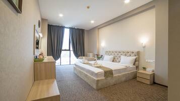 A modern hotel room with a large bed, a bedside table, a nightstand, and a seating area with a bench.