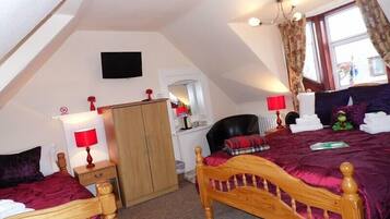 A bedroom with a sloped ceiling, a wooden bed, a wardrobe, a desk with a chair, and a window with curtains.