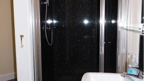 Een badkamer met een douchecabine van glas, een witte wastafel en een spiegel.