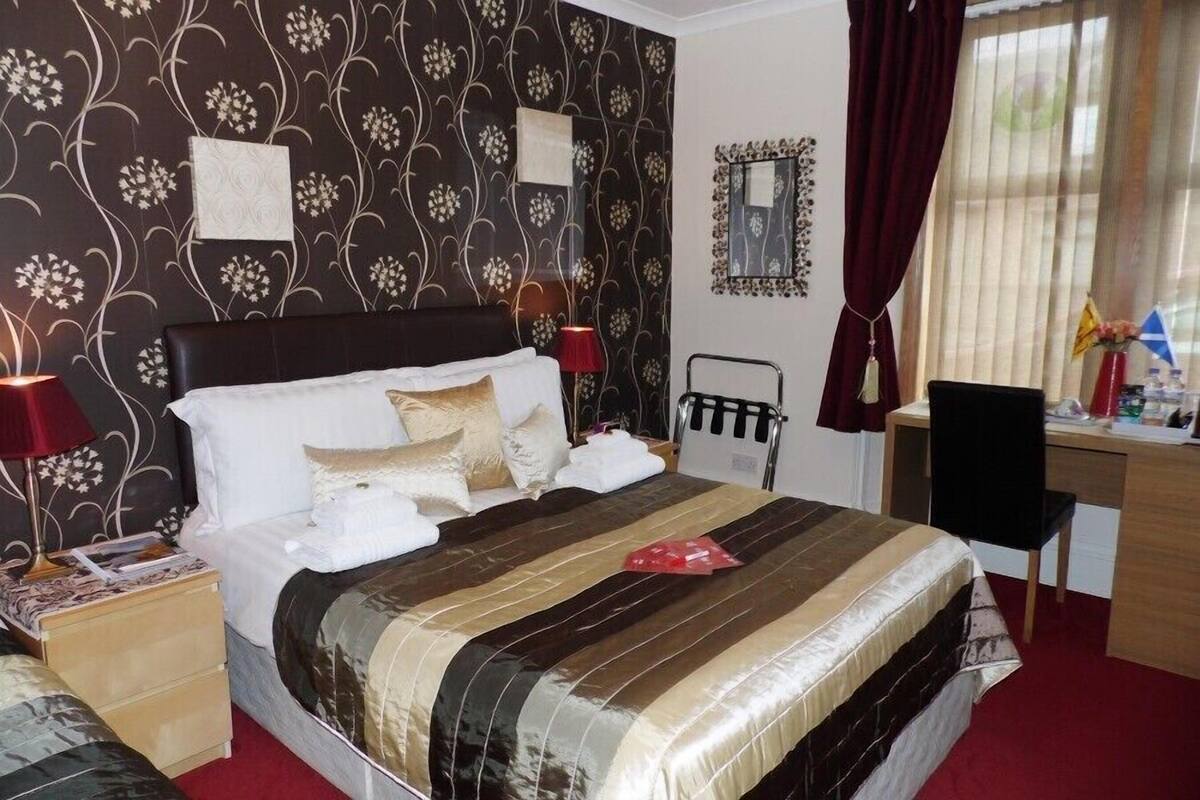 Une chambre d’hôtel avec un grand lit, un bureau et une chaise. Il y a une fenêtre avec des rideaux, une table de chevet avec une lampe et un miroir au mur.