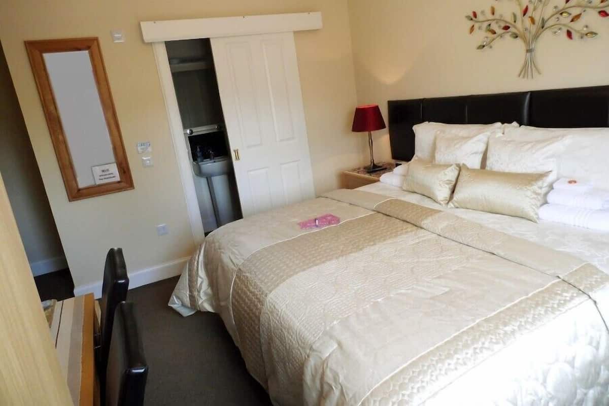Une chambre d’hôtel avec un grand lit, une table de chevet avec une lampe, un miroir et une porte donnant sur une salle de bain.