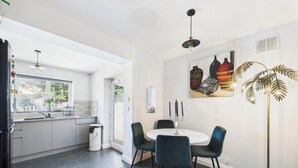 A modern kitchen with a dining area, featuring a round table with chairs, a pendant light, and a wall-mounted artwork. -  Central Serviced Apartments (Cheltenham)