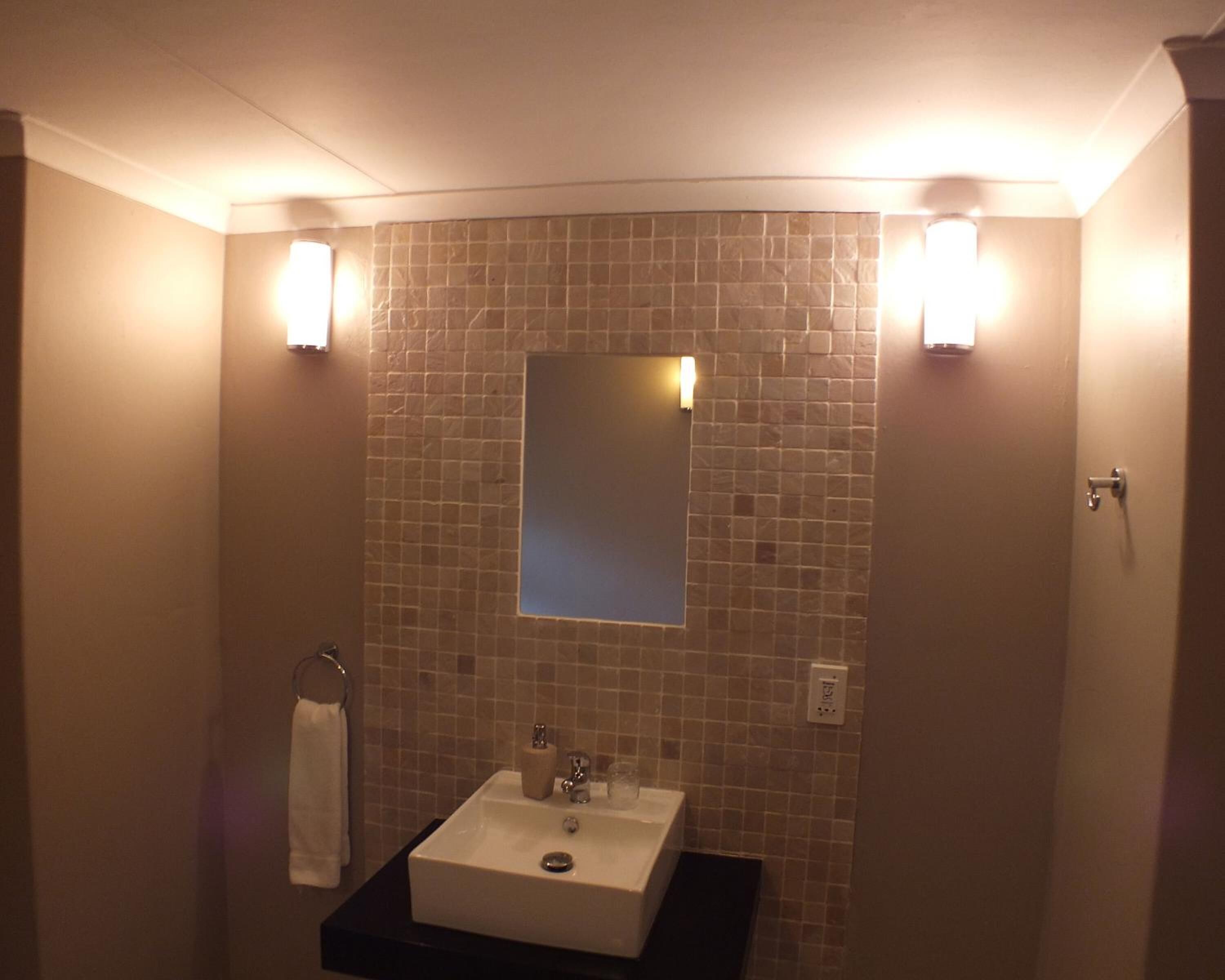 Un baño con un lavabo blanco, un espejo y dos luces fijadas en la pared.