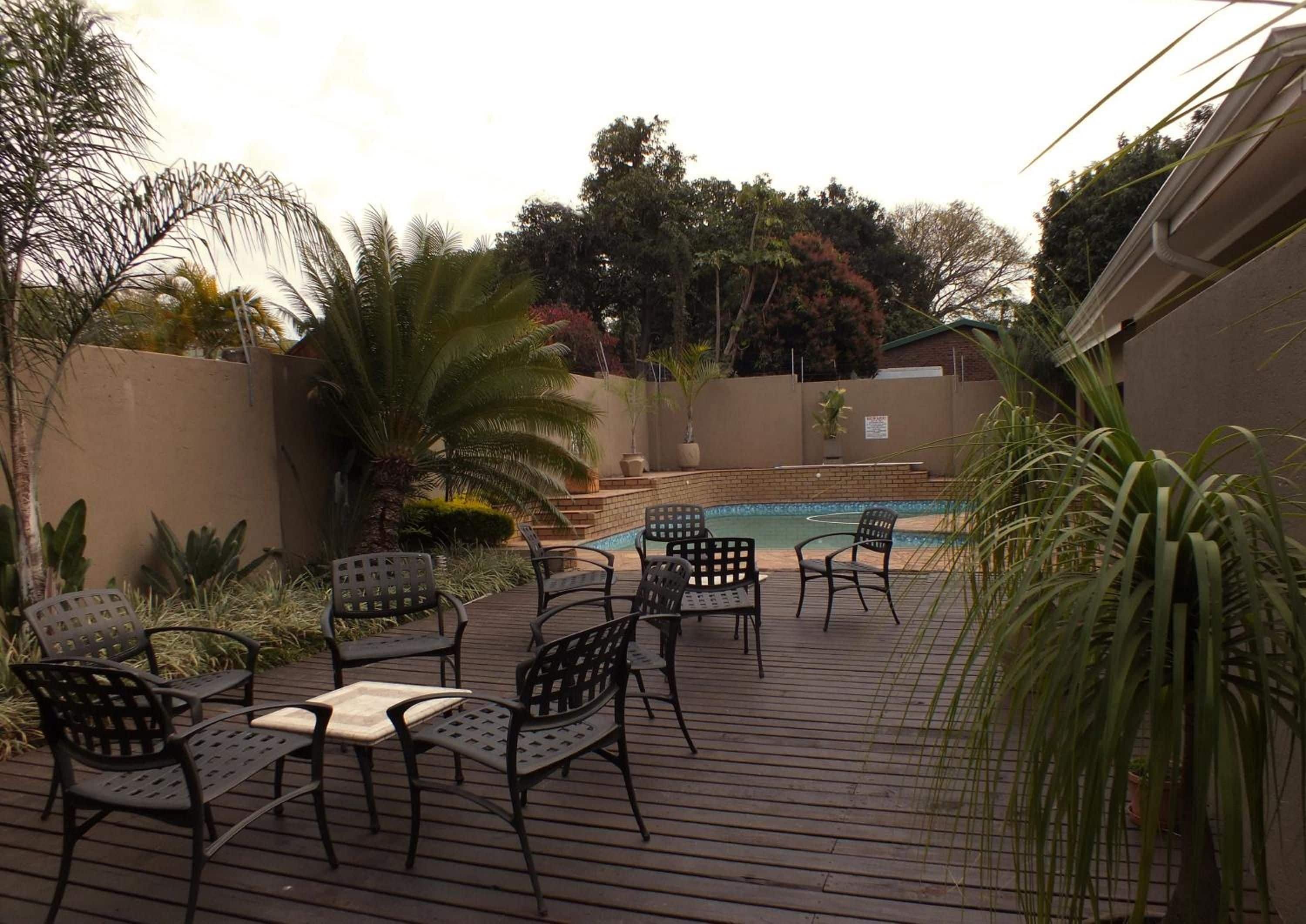 A poolside area with a wooden deck, metal chairs, and a swimming pool.