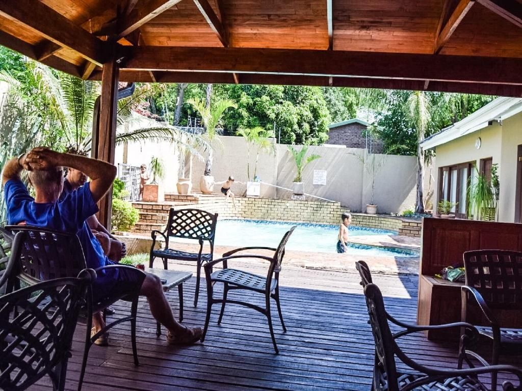 A covered outdoor area with a pool, wooden deck, and chairs.