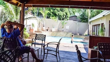 A covered outdoor area with a pool, wooden deck, and chairs.