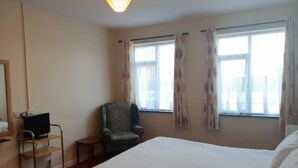 Ein Hotelzimmer mit Bett, Stuhl, Schreibtisch mit Computer und Fenster mit Vorhängen.