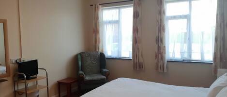 A hotel room with a bed, a chair, a desk with a computer, and a window with curtains.
