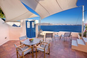 Une terrasse extérieure avec une table et des chaises, une porte bleue et une vue sur la mer.