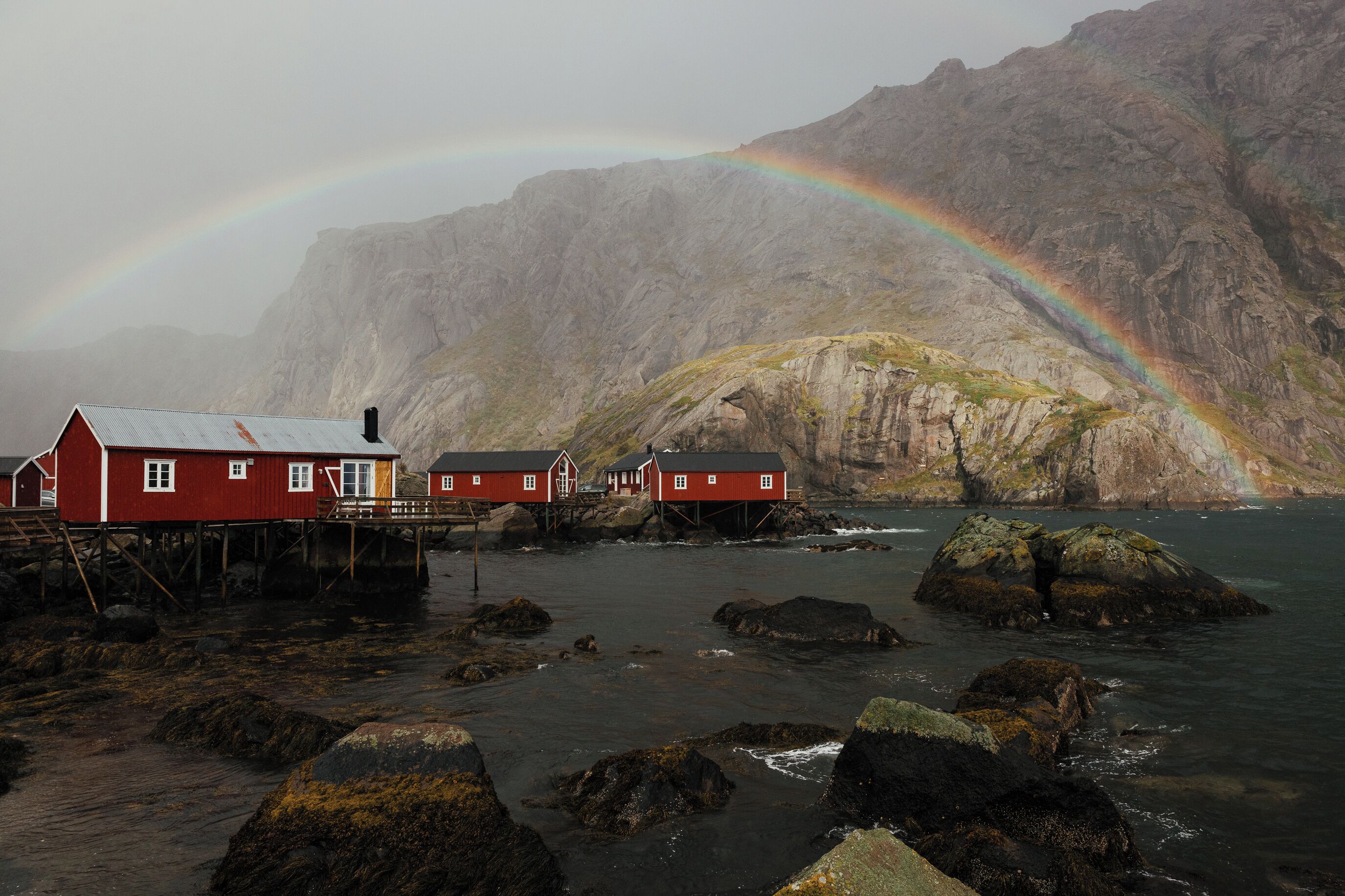 Paisaje costero con casas rojas sobre pilotes, una costa rocosa y una montaña al fondo.