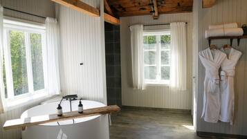 A bathroom with a bathtub, wooden beams, white walls, and a window with curtains.