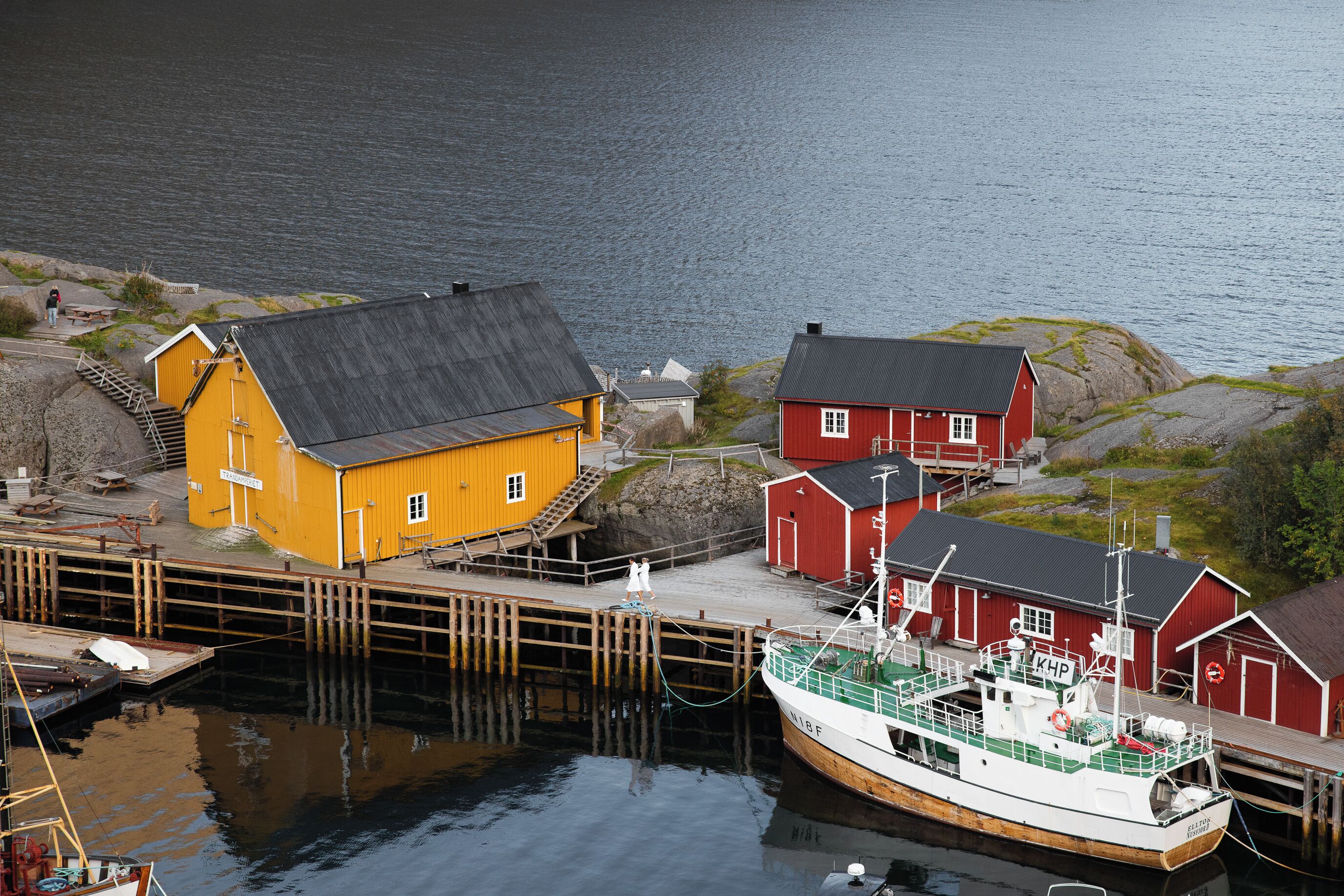 A harbor with a yellow building, a red building, and a boat docked at the pier.