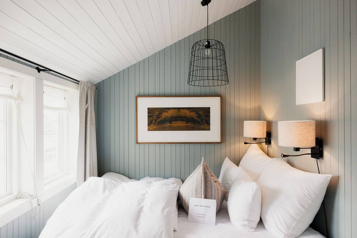 Un dormitorio con cama, un cuadro enmarcado, dos lámparas de pared y una ventana con cortinas.