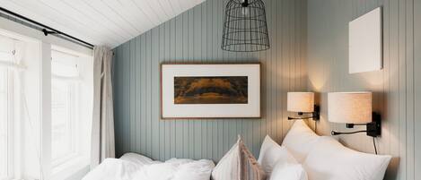 A bedroom with a bed, a framed picture, two wall-mounted lamps, and a window with curtains.
