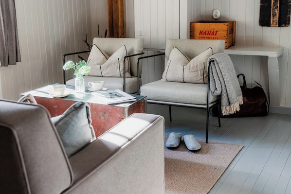 Una sala de estar moderna con un sofá, dos sillones, una mesita de centro y una pequeña estantería.