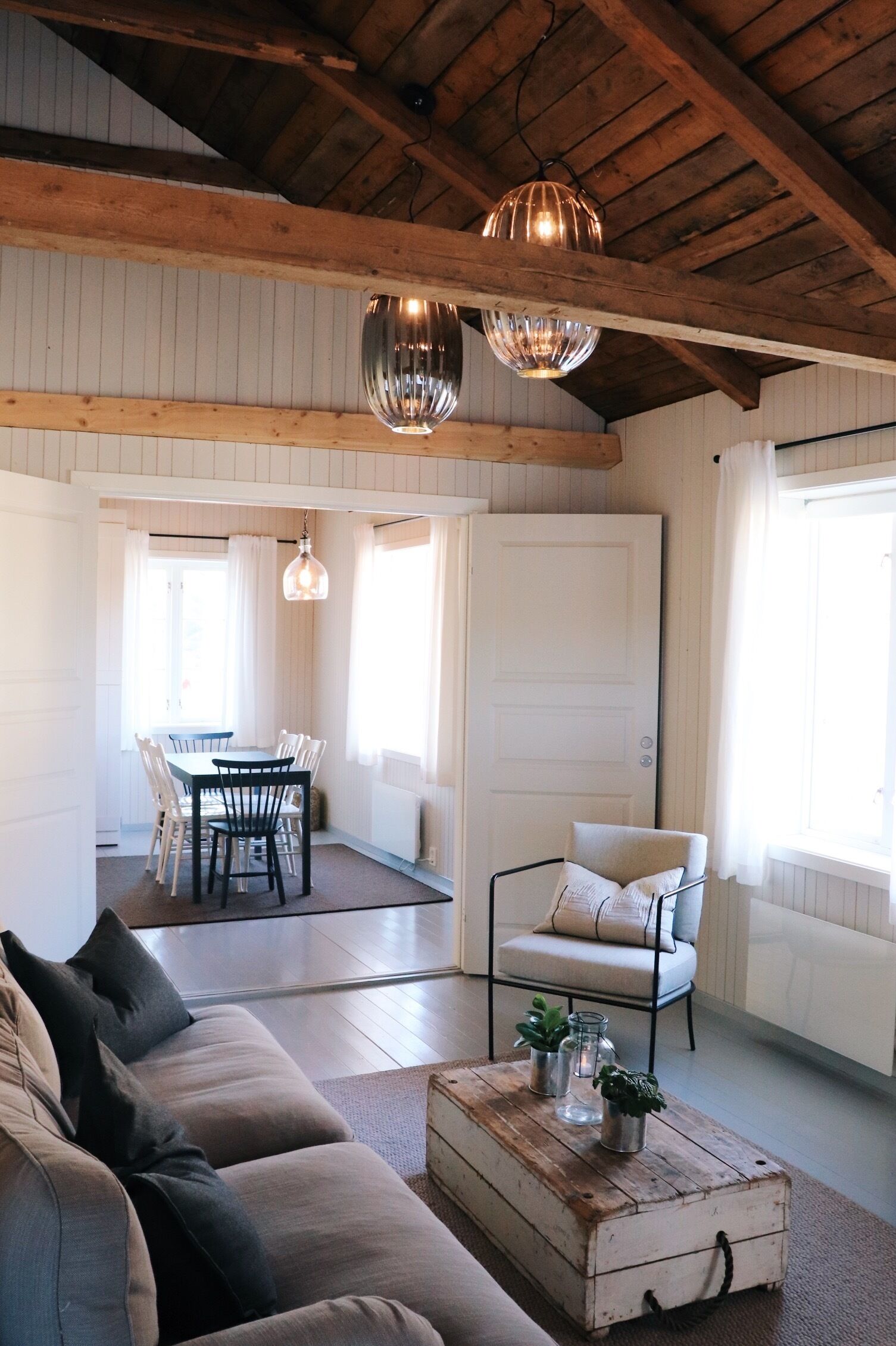Ampla sala de estar com teto de madeira, mesa de jantar com cadeiras, sofá e mesa de centro com objetos decorativos.