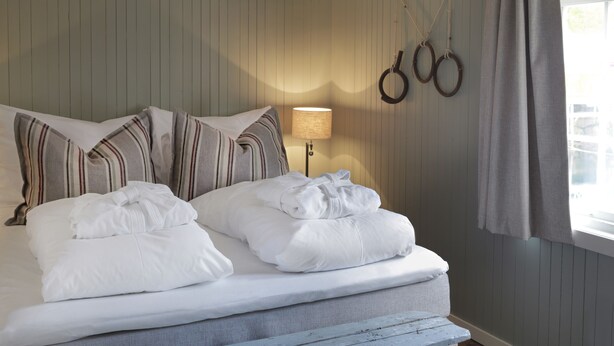 A neatly made bed with striped pillows, a lamp, and rings on the wall. - Nusfjord Village & Resort (Flakstad)