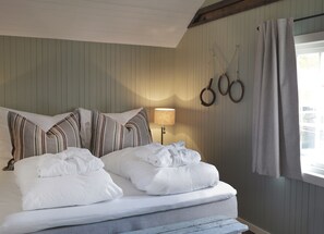 Una cama bien hecha con almohadas a rayas, una lámpara y anillos en la pared.