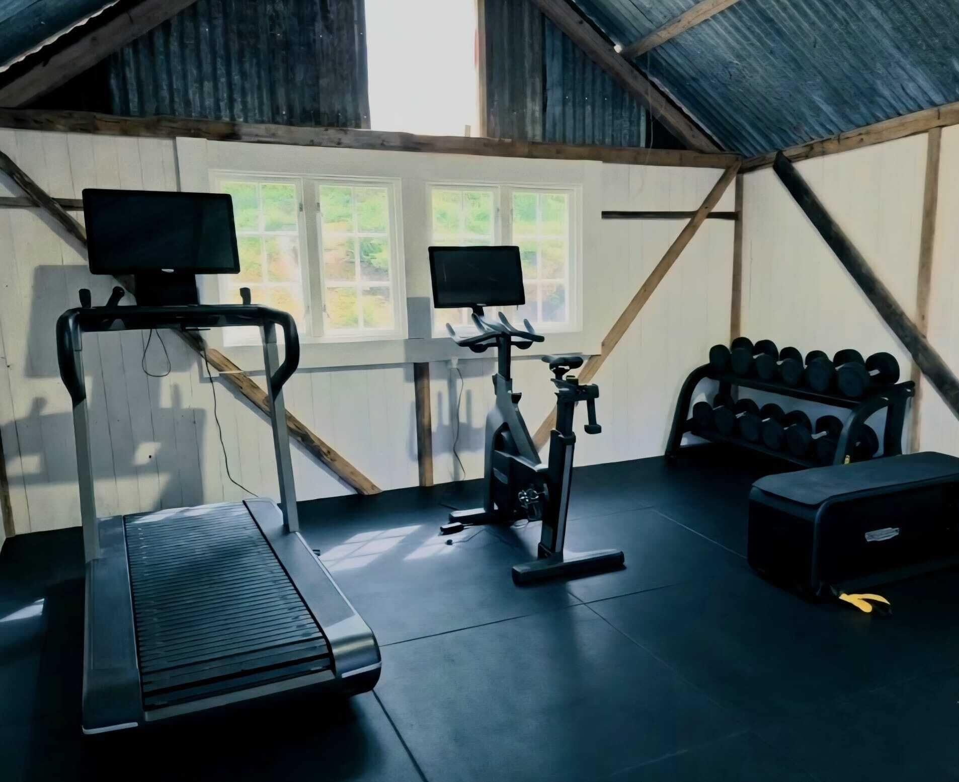 Een sportschool met een loopband, een hometrainer en gewichten.