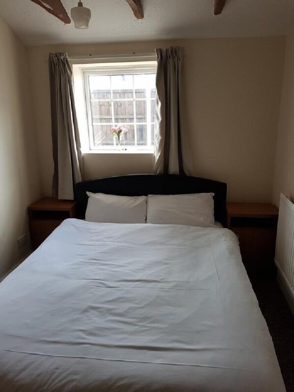 A neatly made bed in a room with a window, curtains, and a radiator.