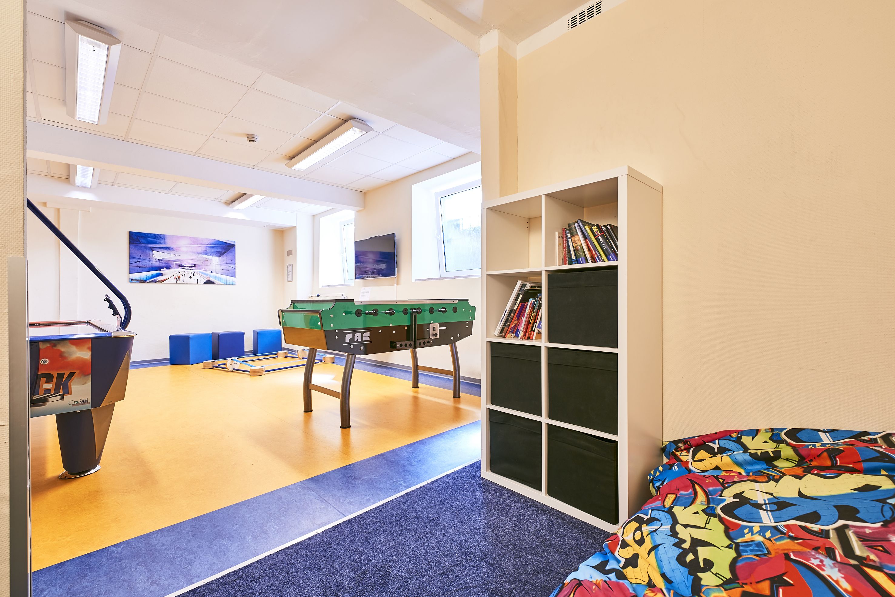 Una habitación con mesa de fútbol de mesa, una estantería y una cama con una manta de colores.