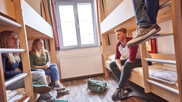 Ein Schlafsaalzimmer mit Etagenbetten, einem Fenster und einer Heizung.