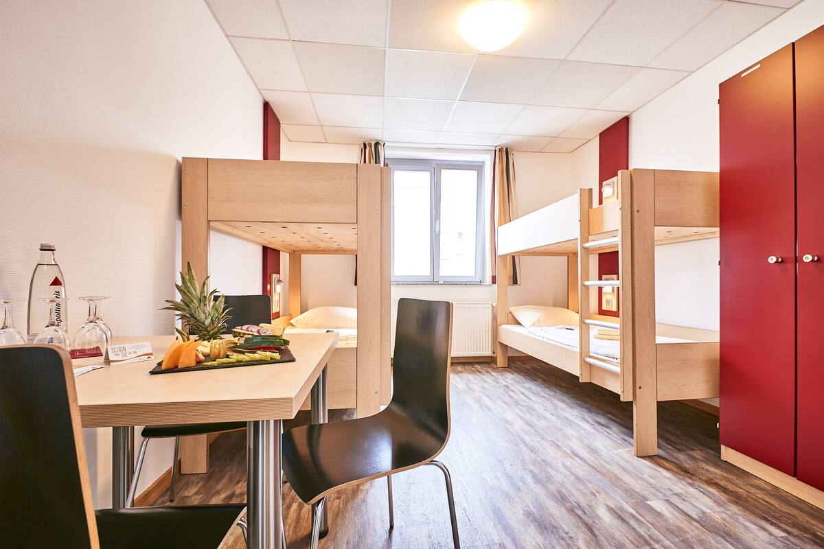 Un dormitorio con literas, una mesa de comedor con sillas y una ventana.