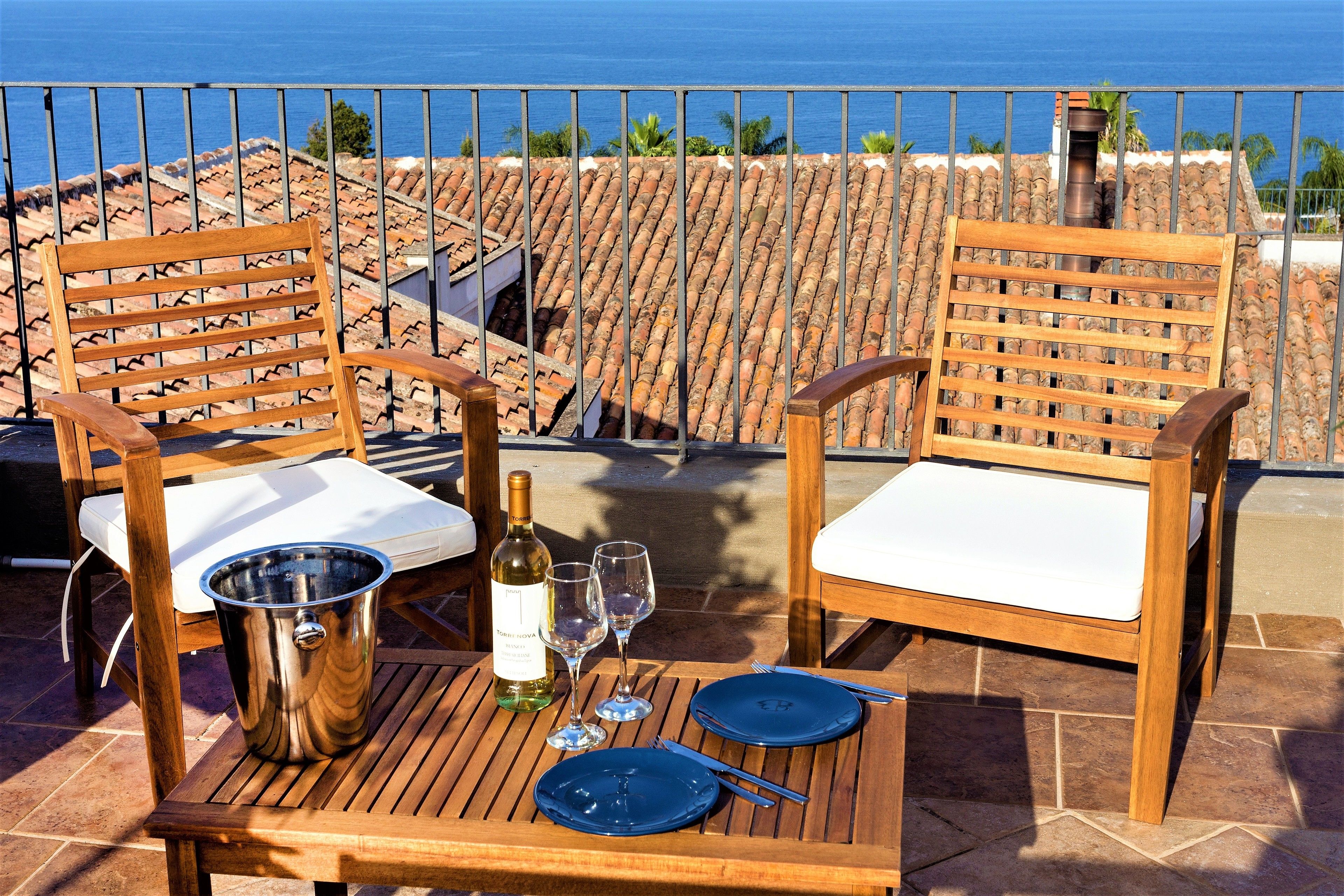 Una terrazza con due sedie di legno, un tavolo, una bottiglia di vino e dei bicchieri.