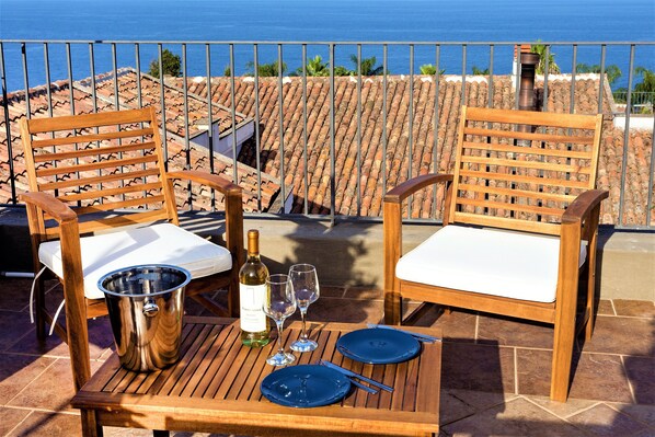 A terrace with two wooden chairs, a table, a wine bottle, and glasses.