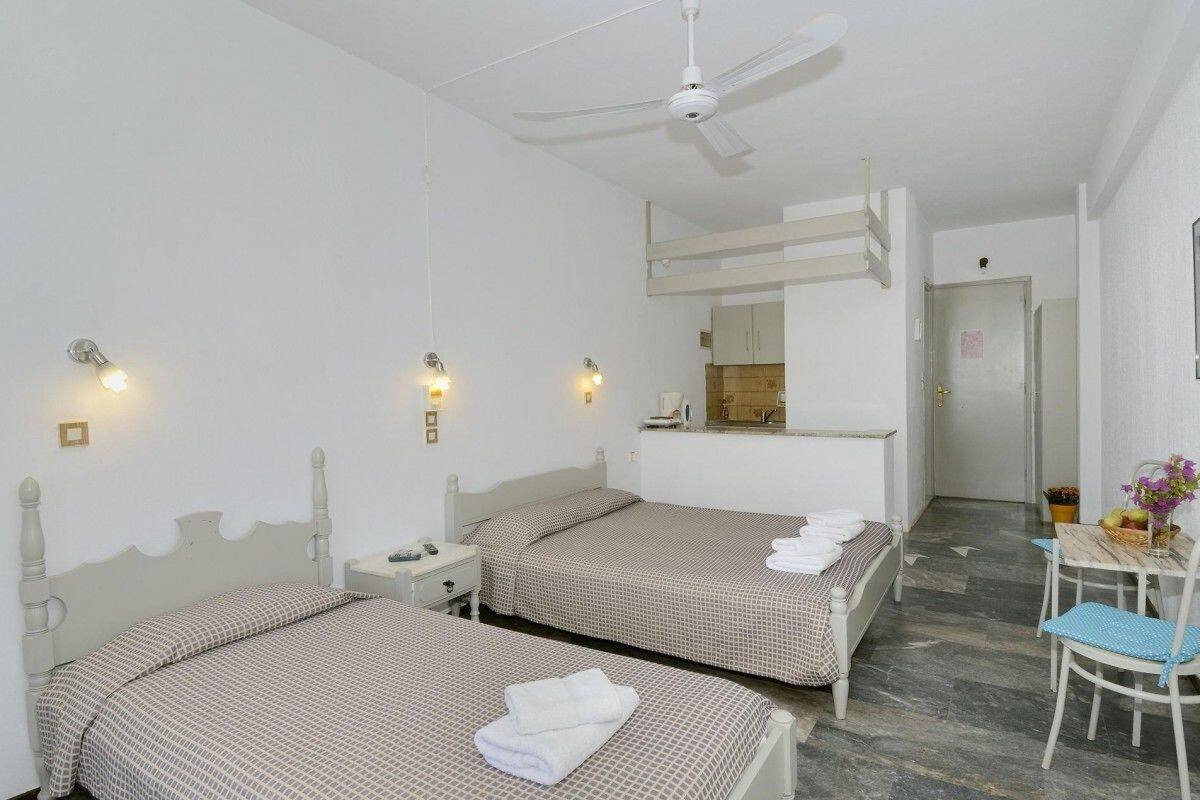 A hotel room with two beds, a desk, a chair, a ceiling fan, and a small table with a vase of flowers.
