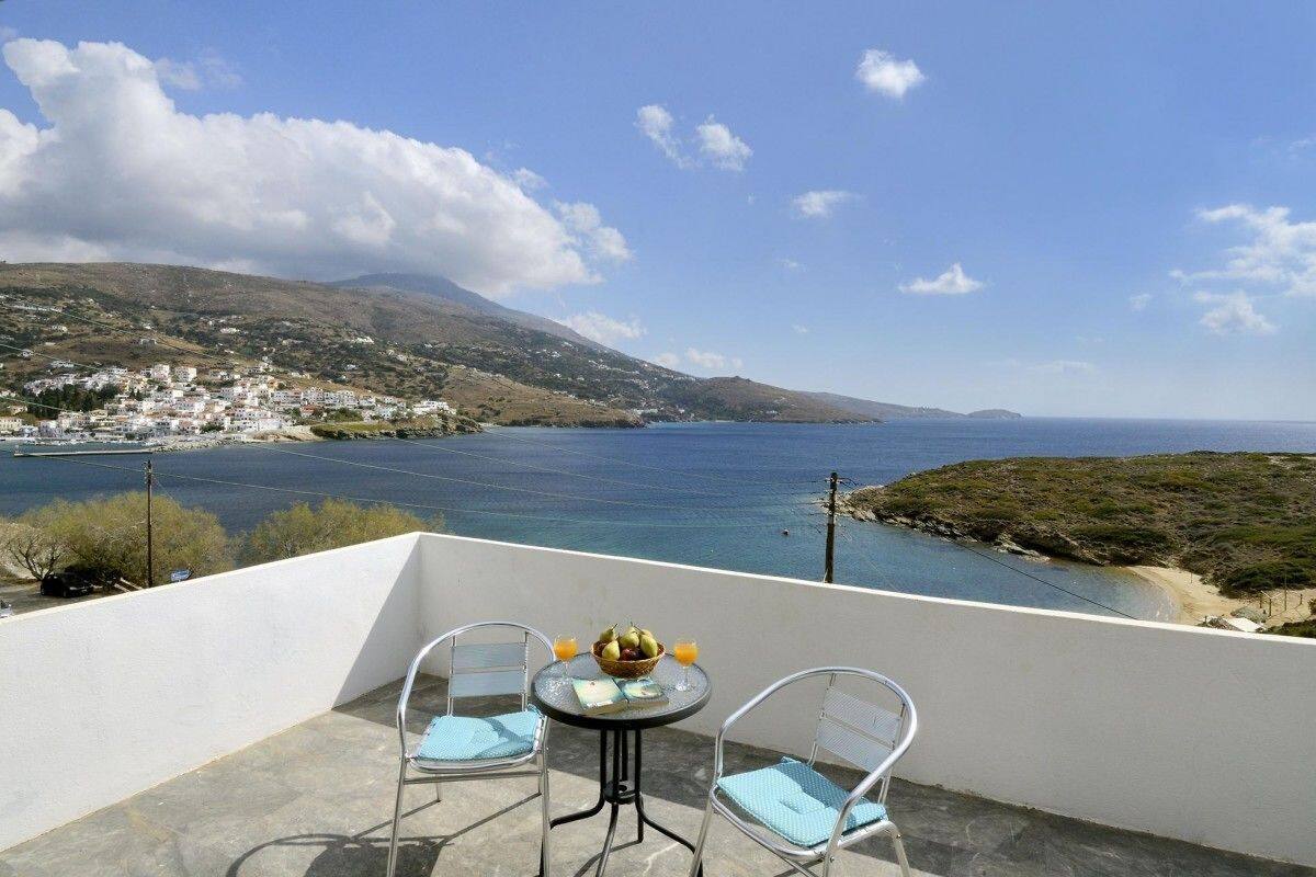 A balcony with two chairs and a table, overlooking a coastal town and the sea.
