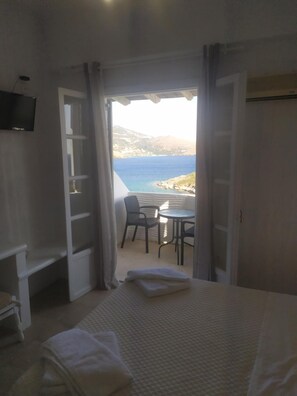 A bedroom with a bed, a TV, a desk, and a view of the sea.