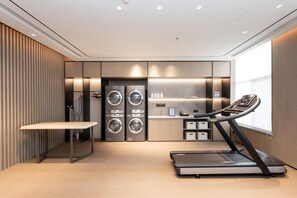Quarto de hotel moderno com esteira ergométrica, máquinas de lavar roupa e uma toucador com espelho.