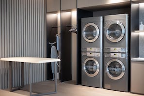 A modern laundry room with four stacked front-loading washers and dryers, a mirror, and a small ironing station.
