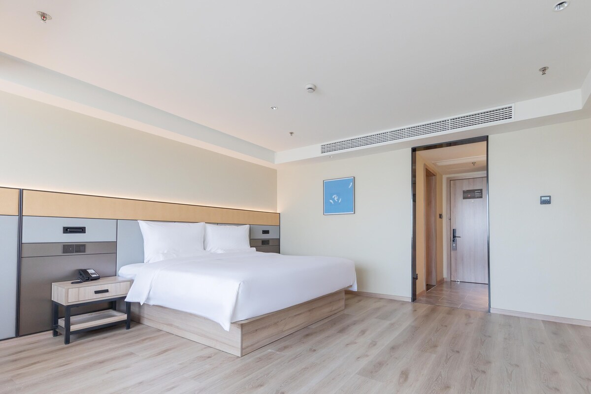 Quarto de hotel com cama, mesa de cabeceira e porta que dá para outro cômodo.