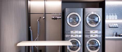 A modern laundry room with two front-loading washing machines, a drying rack, and a small table.
