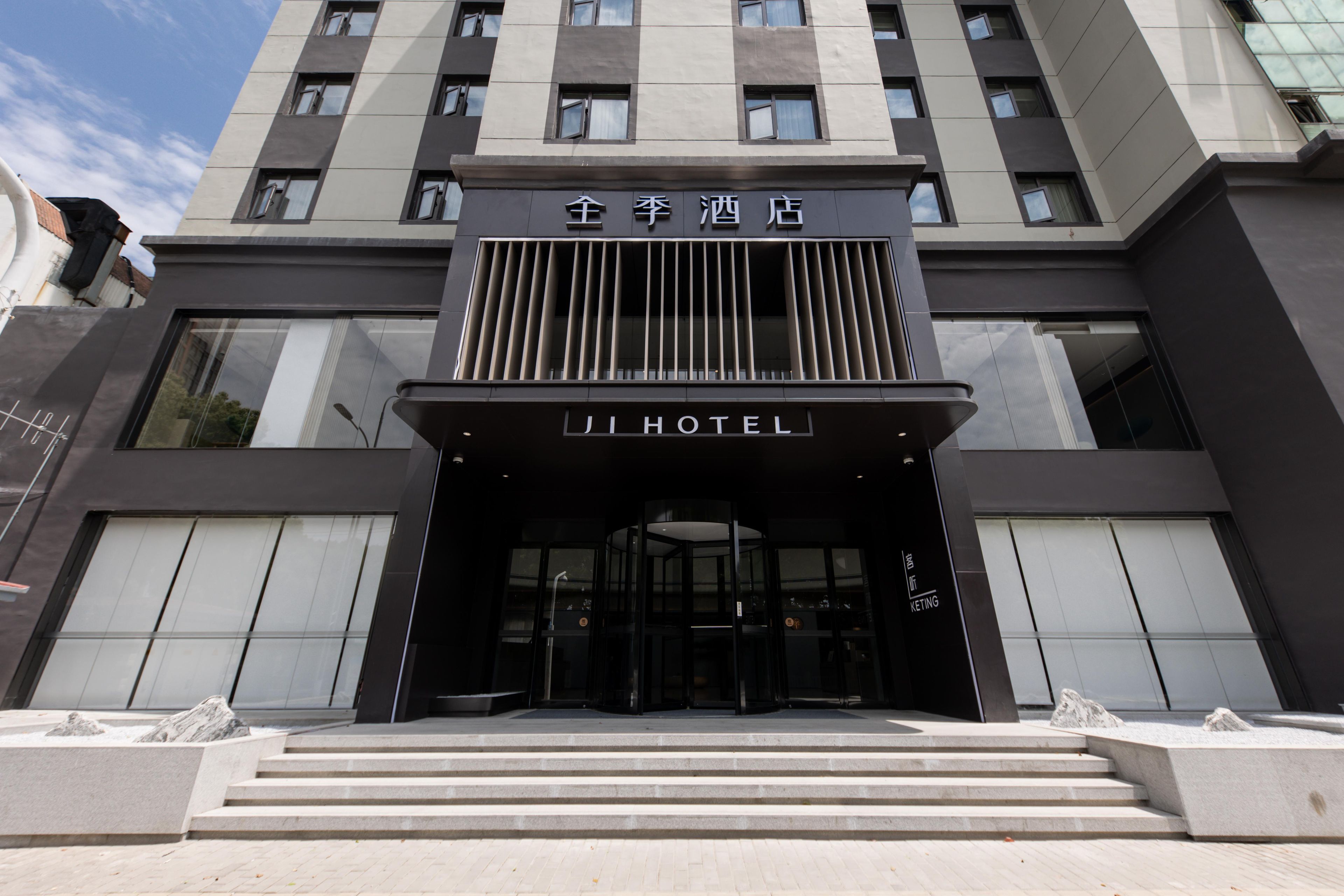 A modern hotel entrance with a prominent sign, a set of steps leading up to the entrance, and a glass facade.