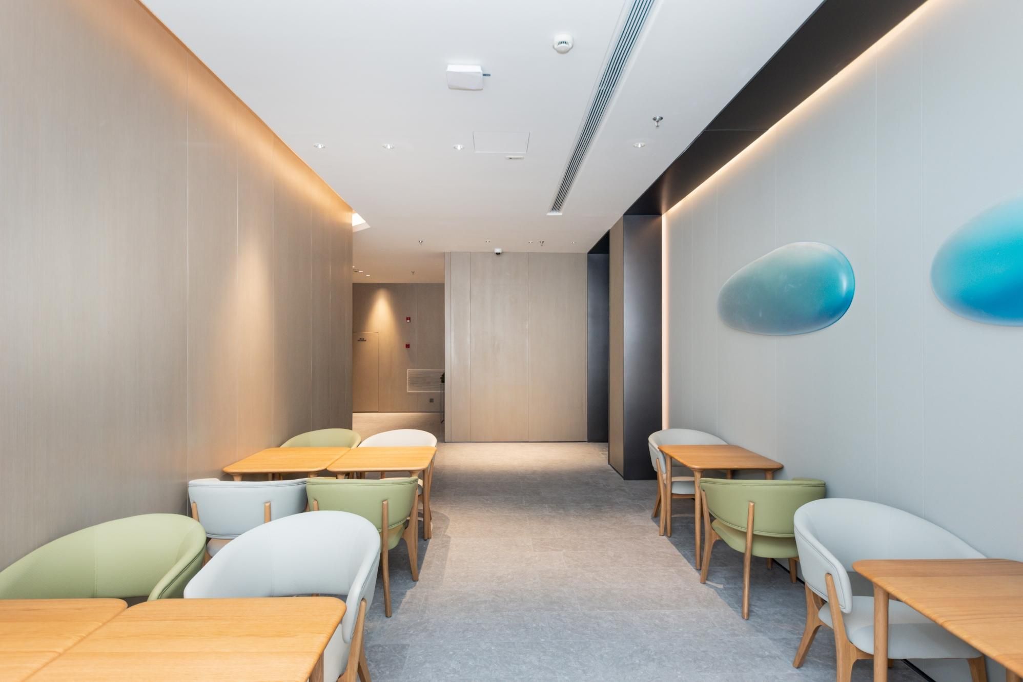 A modern conference room with tables and chairs, a white ceiling with recessed lighting, and a blue decorative element on the wall.