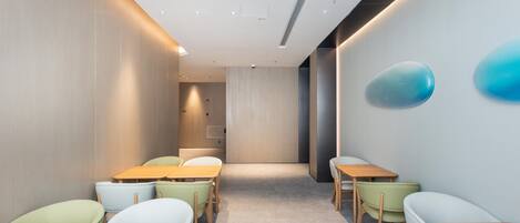 A modern conference room with tables and chairs, a white ceiling with recessed lighting, and a blue decorative element on the wall.