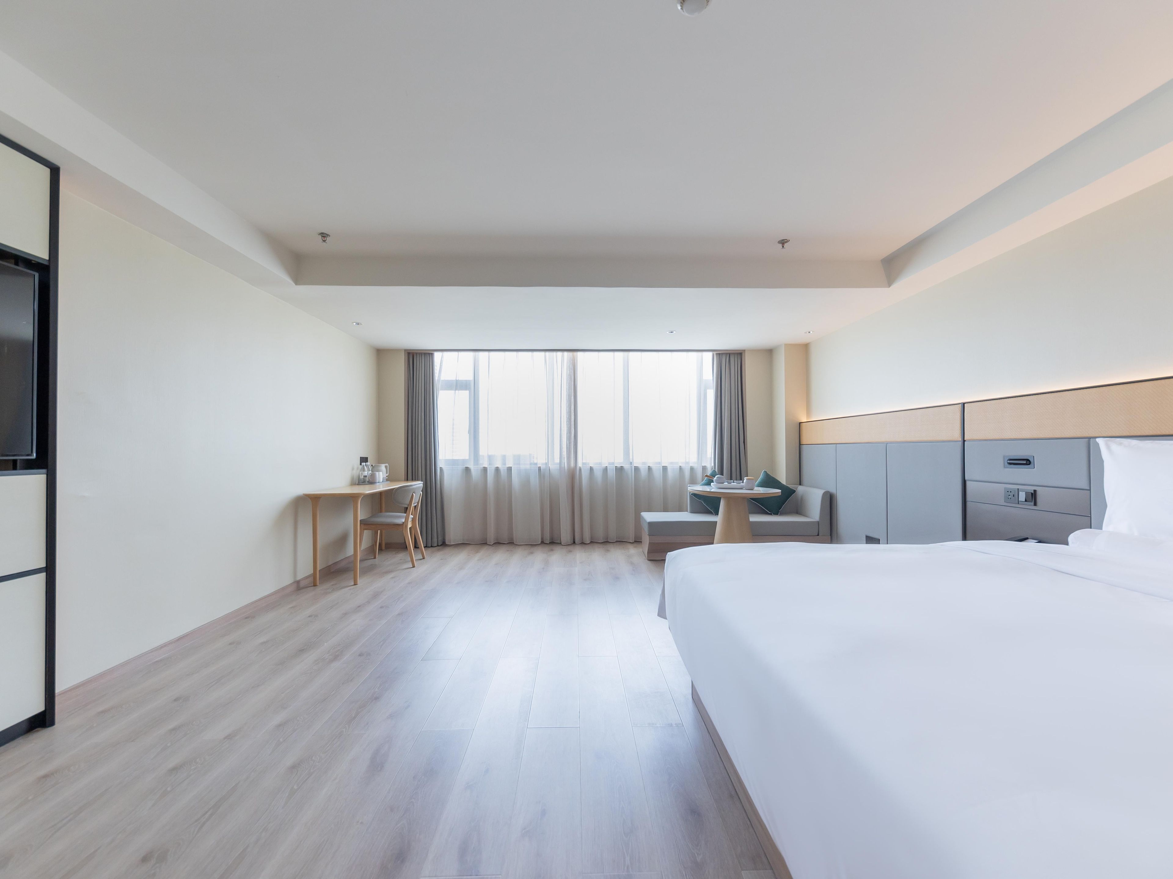 A hotel room with a bed, a desk, a chair, a small table, and a TV.