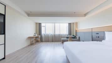 A hotel room with a bed, a desk, a chair, a small table, and a TV.