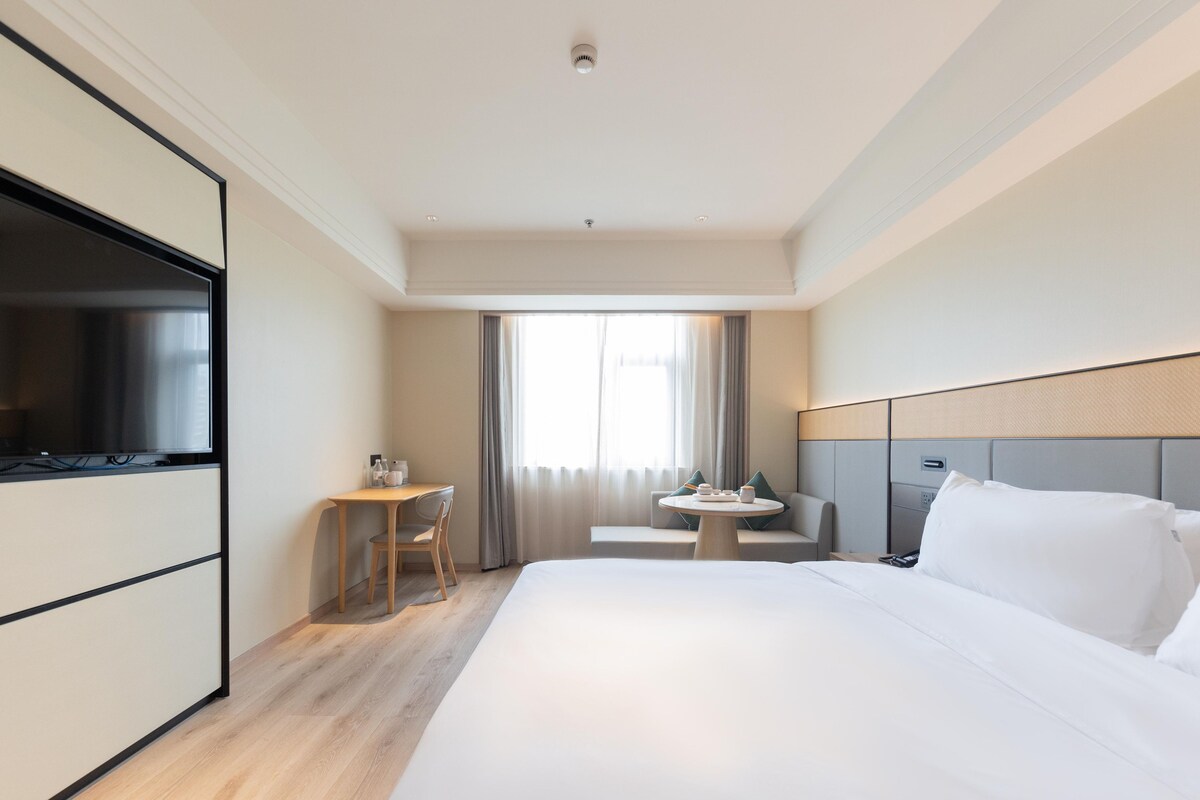 Quarto de hotel com cama, escrivaninha, cadeira, mesa e televisão.