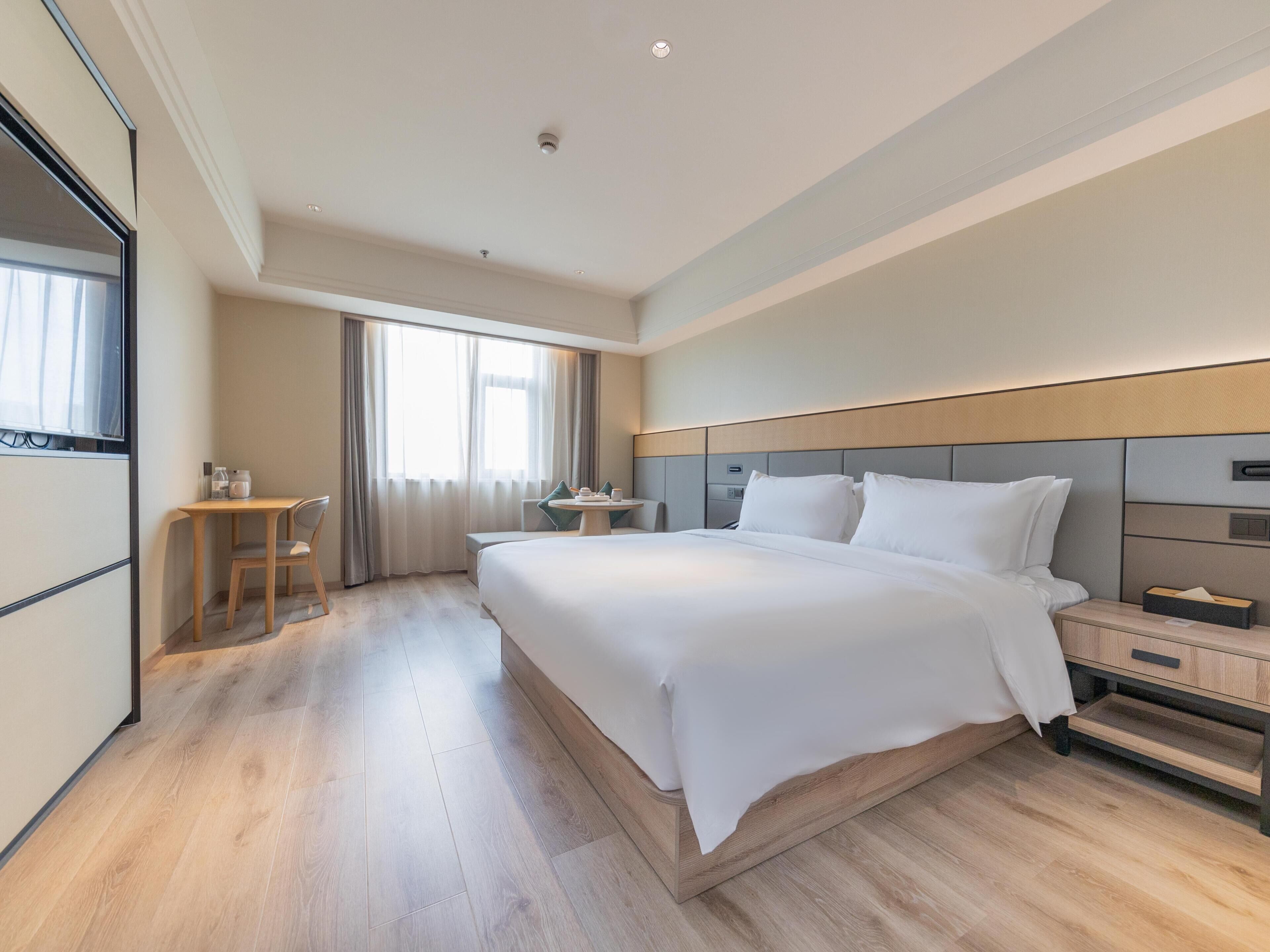 A hotel room with a large bed, bedside tables, a small desk, and a window with curtains.