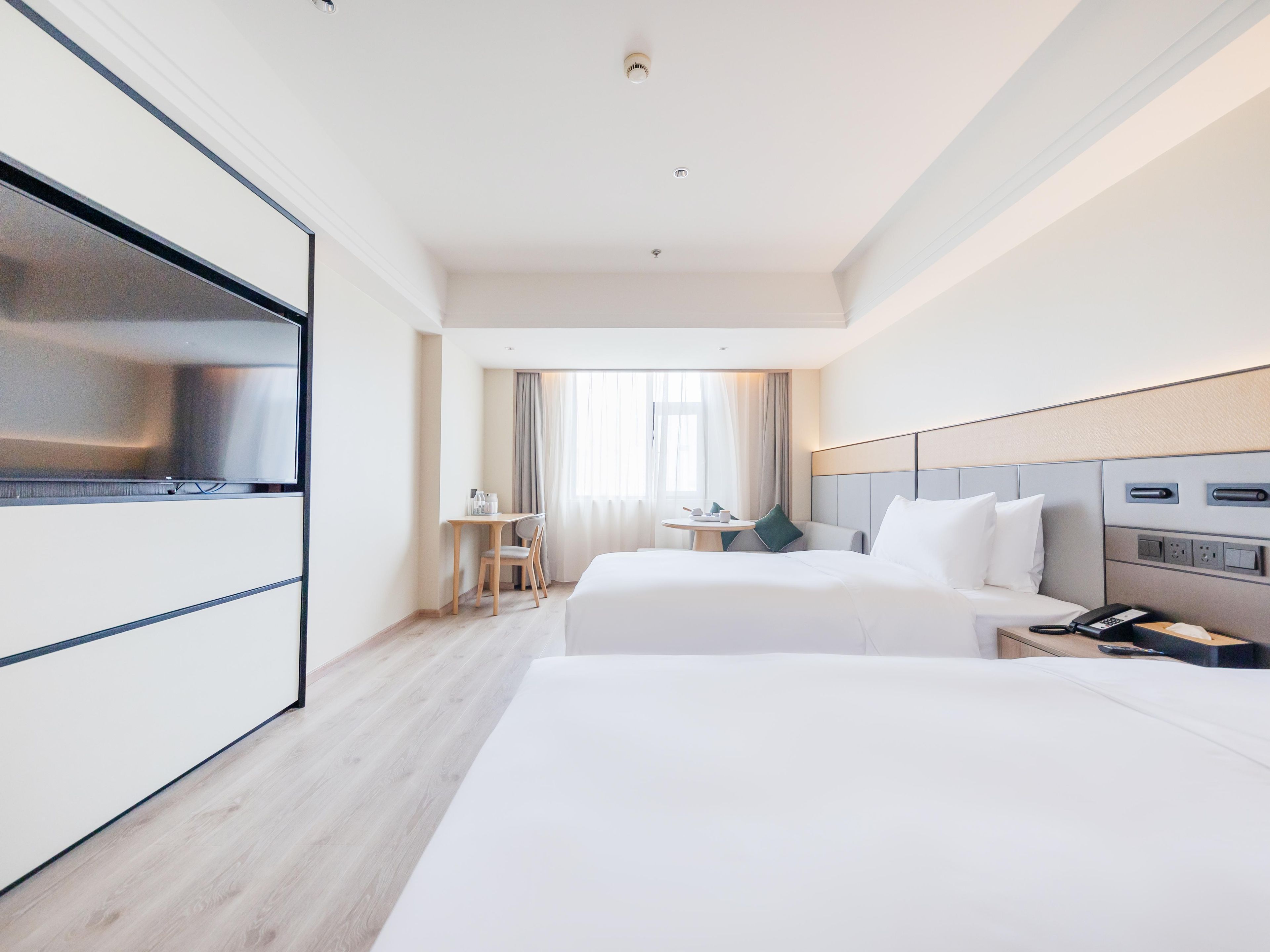 A hotel room with two beds, a desk, a chair, a TV, and a phone.